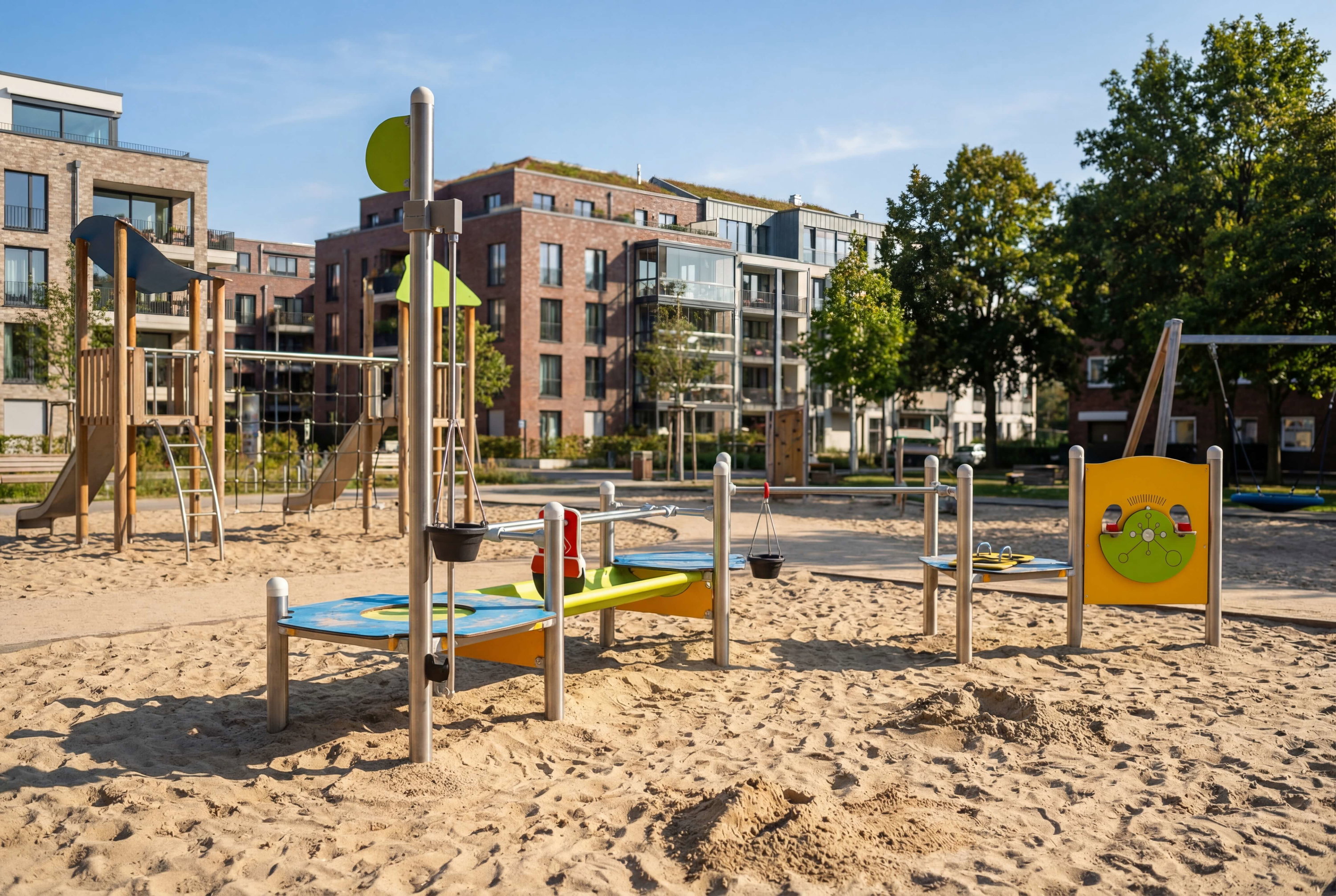 Spielplatz mit Sand und modernen Wohnhäusern im Hintergrund unter blauem Himmel.