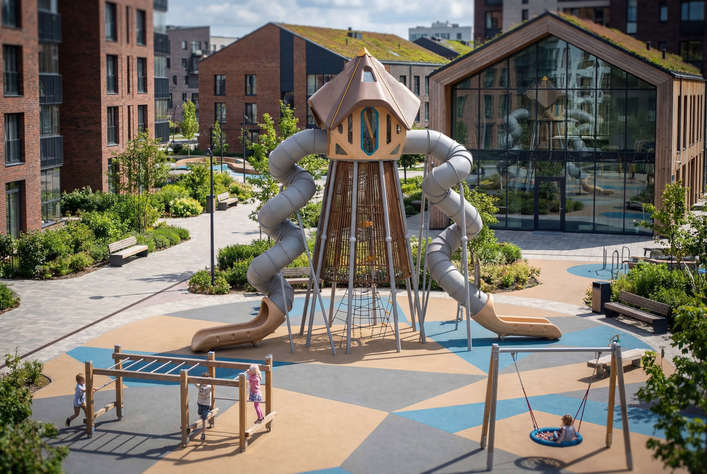 Kinder spielen auf einem modernen Spielplatz mit Rutschen und Klettergerüsten vor Wohnhäusern.