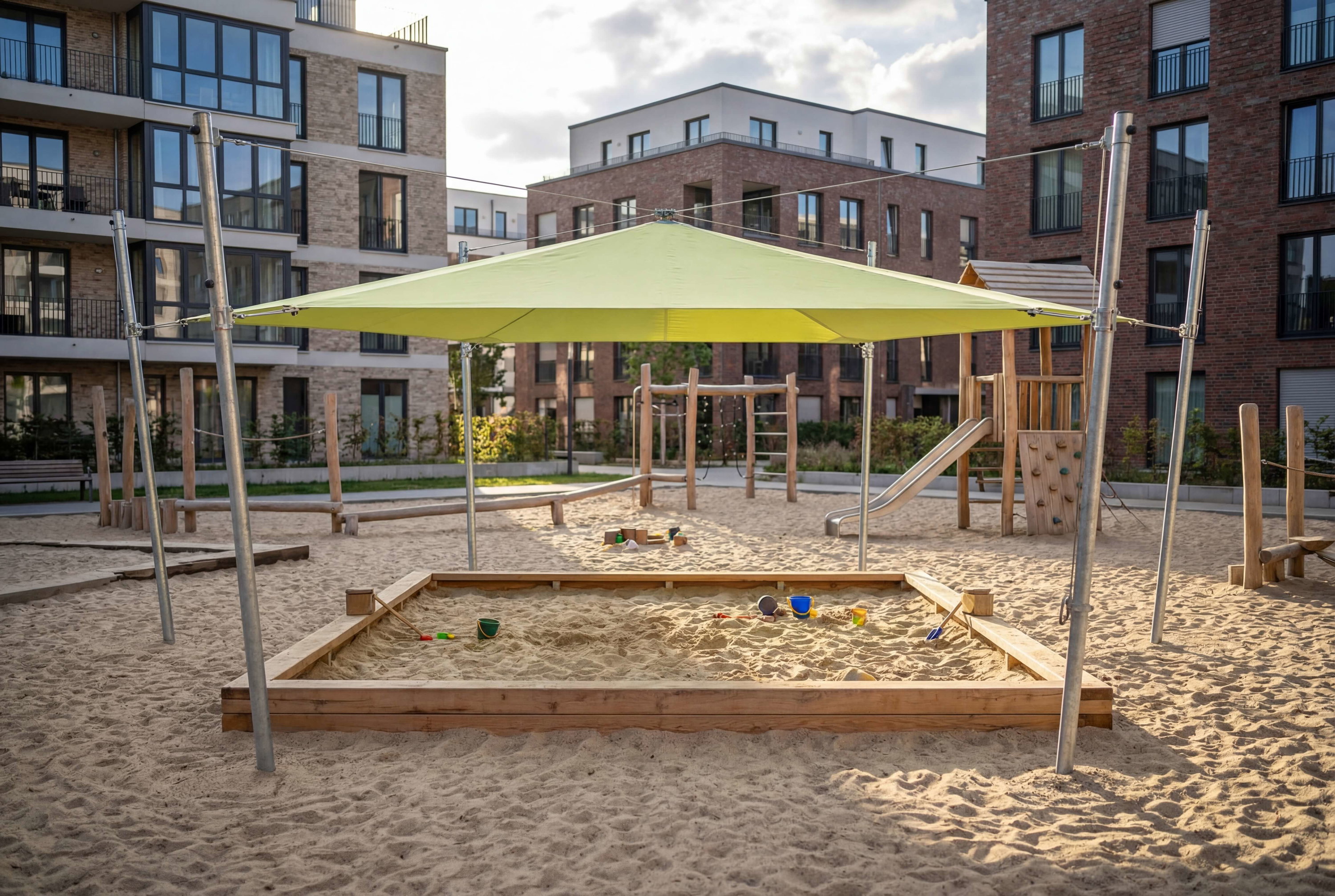 Spielplatz mit Sandkasten und Schutzdach vor modernen Wohnhäusern.