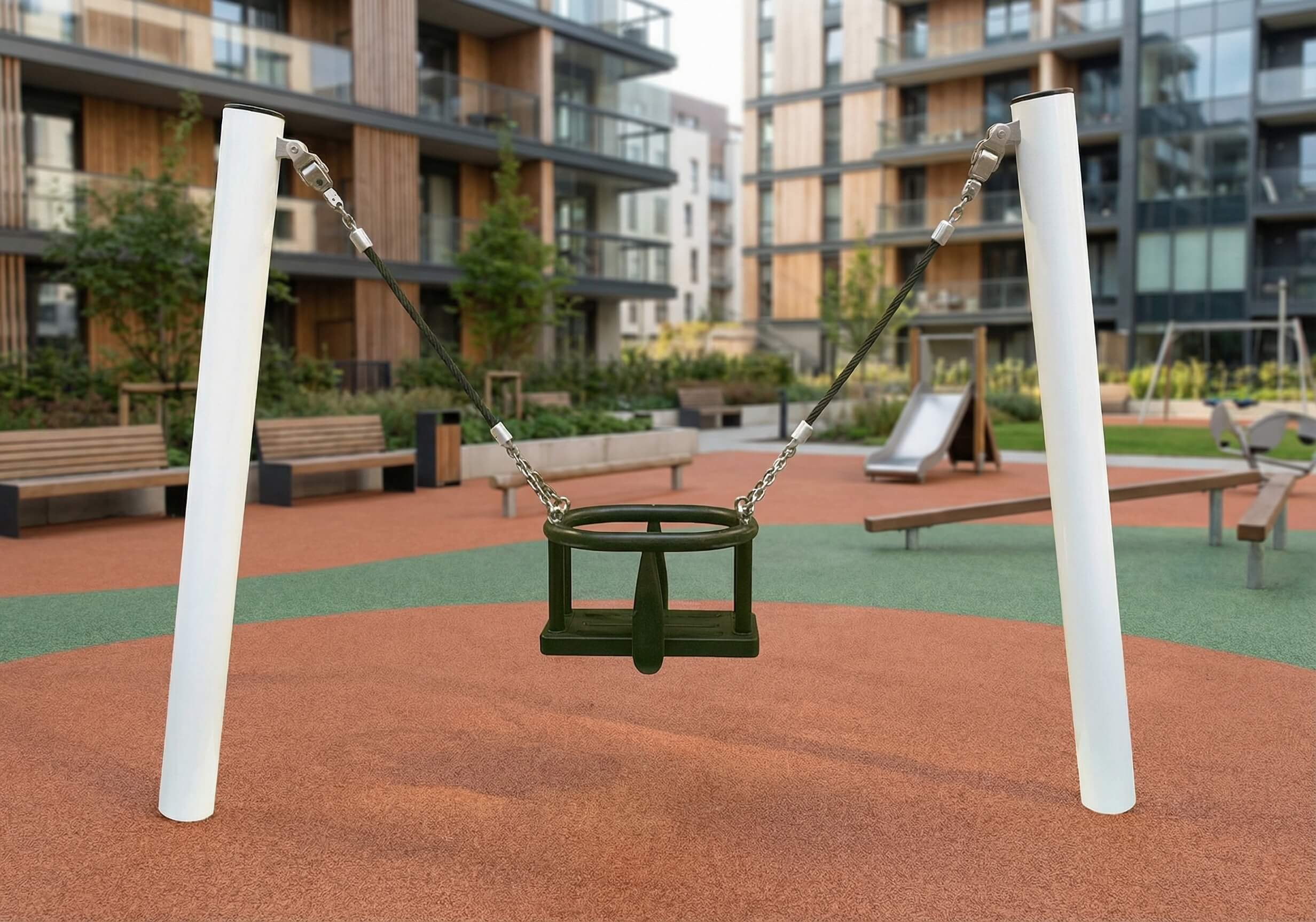 Ein grüner Rundschaukel im modernen Spielplatz vor Wohnhäusern mit Sandboden und Bänken.