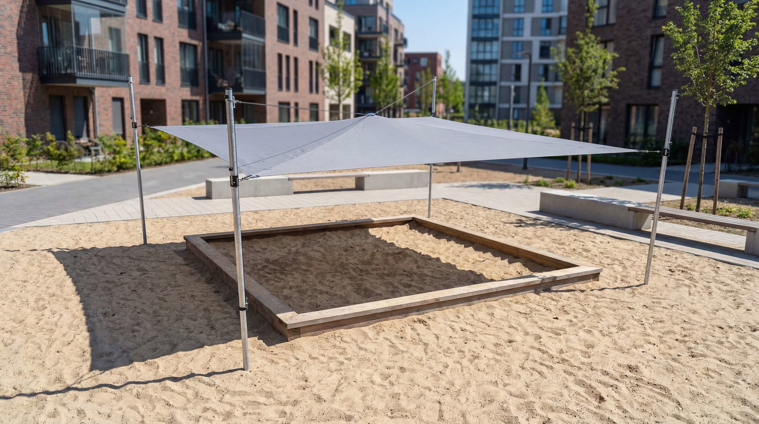 Spielplatz mit Sandkasten und Sonnensegel im modernen Wohngebiet unter blauem Himmel.