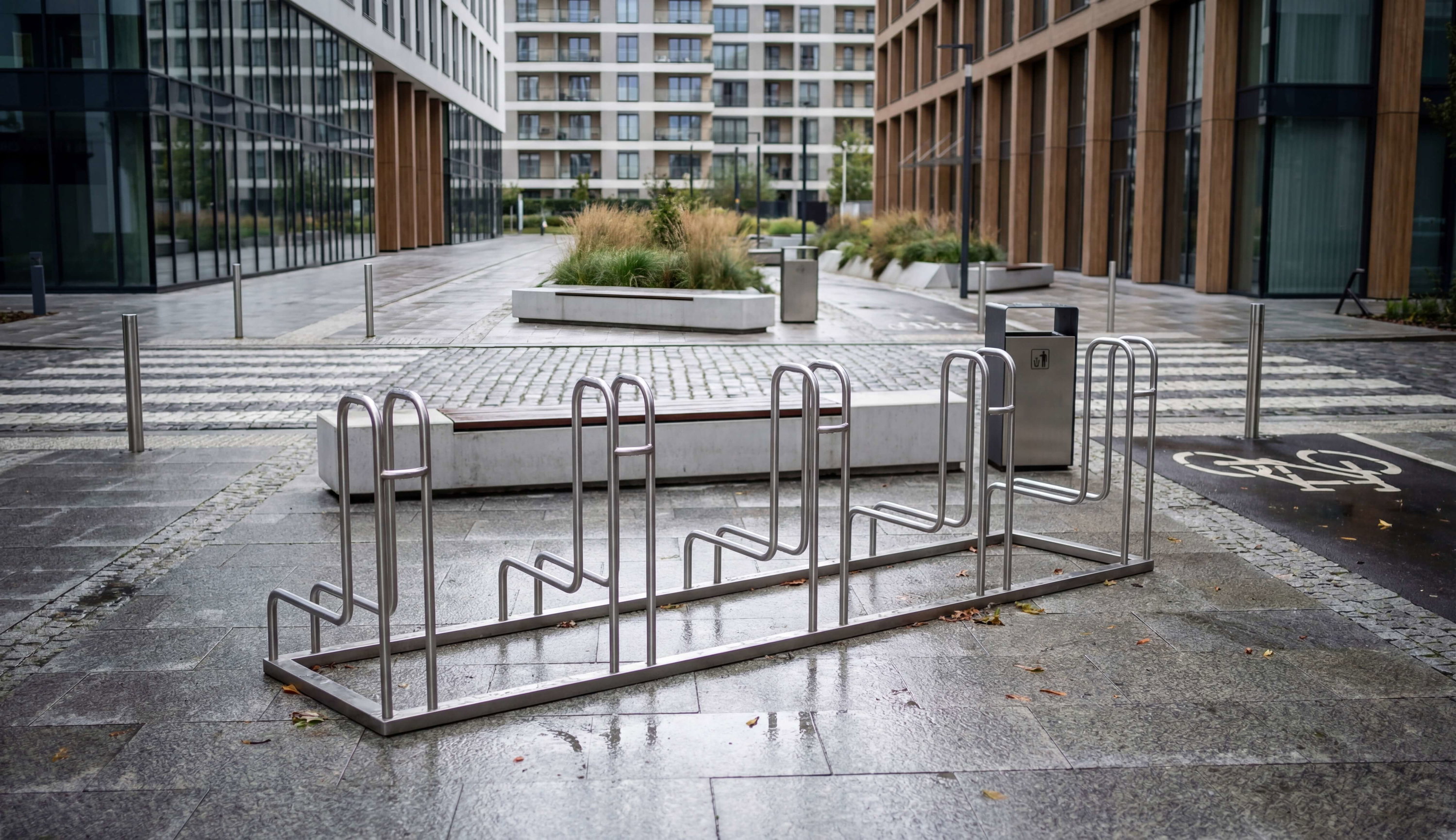 Leere Fahrradständer im modernen Bürokomplex mit nassen Pflastersteinen und Glasfassaden.