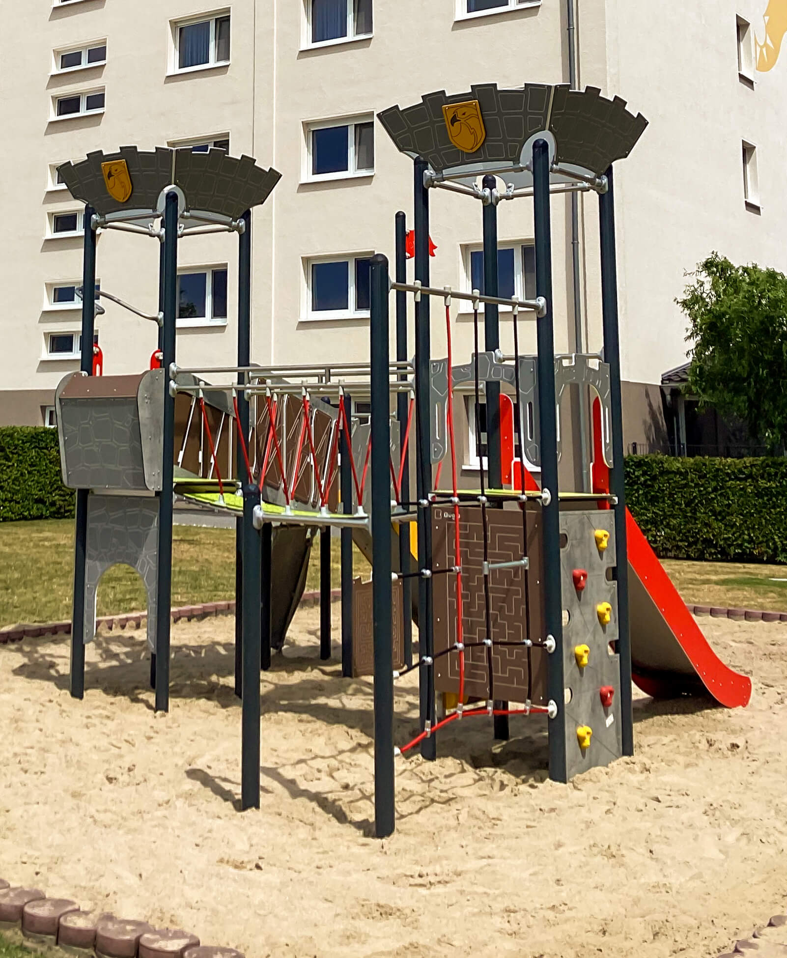 Kinder-Spielplatz mit Rutsche und Kletterwand im Sand vor Wohnhaus