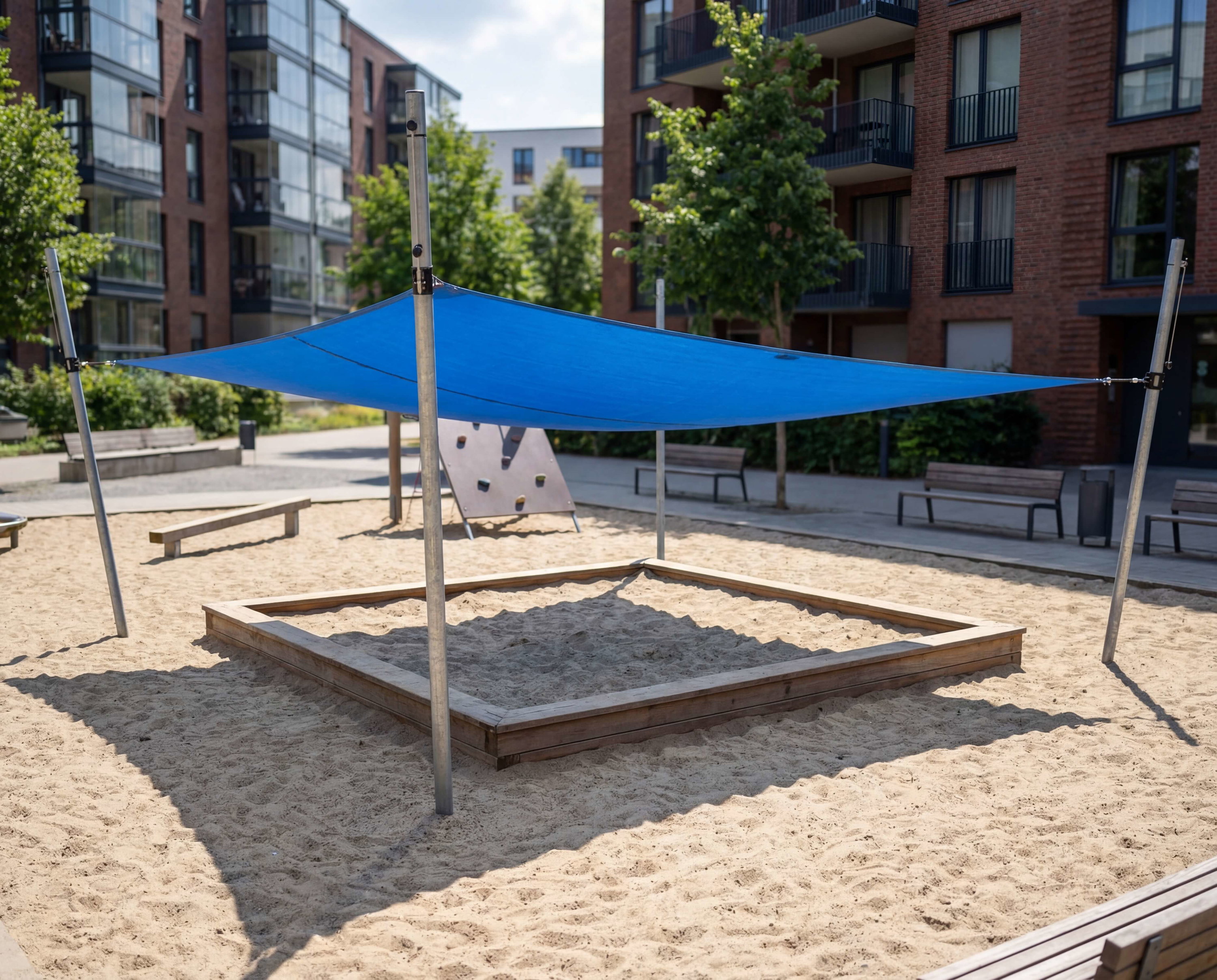 Blauer Schattenspender über Sandkasten im Spielplatz vor Wohnhäusern.