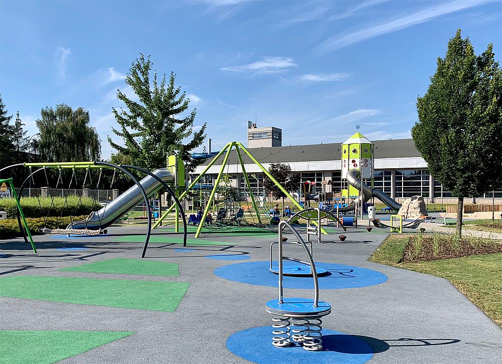 Farbechter Spielplatz mit Rutschen und Schaukeln vor Schulgebäude unter blauem Himmel.