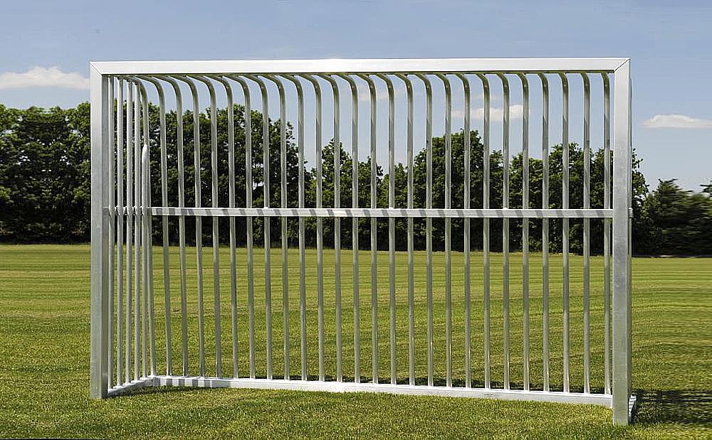 Metallzaun im Gras vor Bäumen unter blauem Himmel