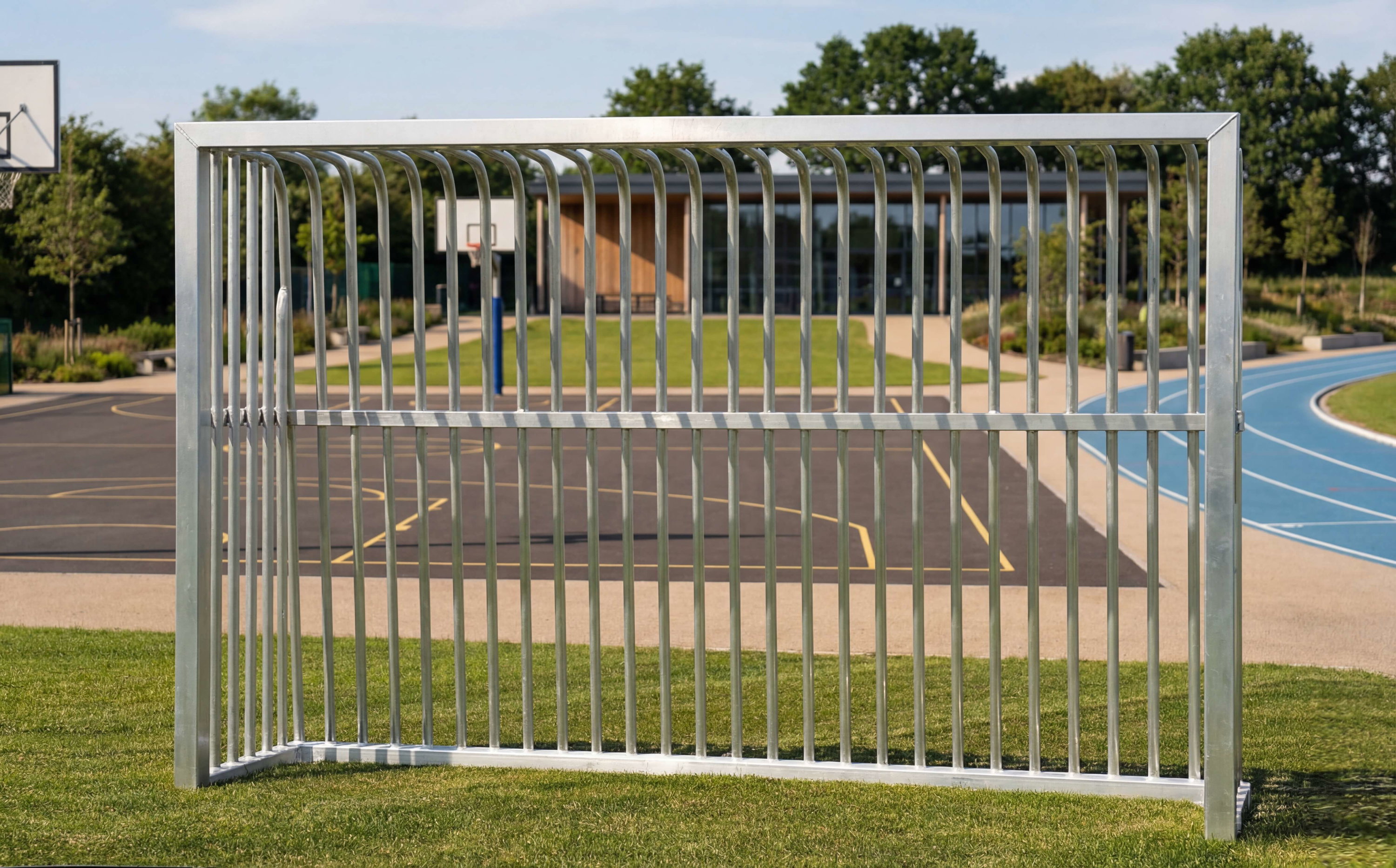 Metalltor auf Gras vor Sportplatz mit Basketballkorb und Laufbahn im Hintergrund.