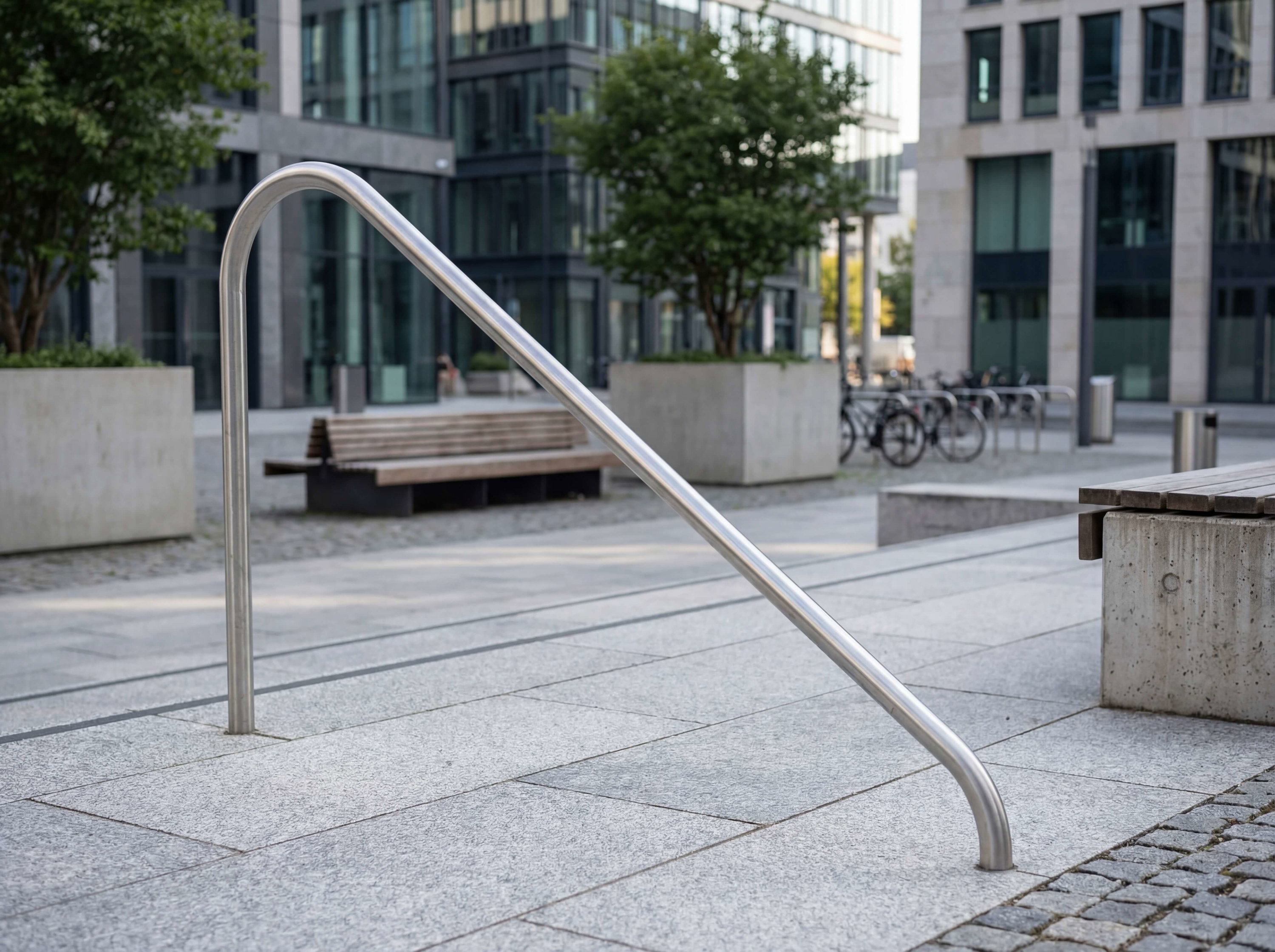 Stahlhandlauf im modernen Stadtplatz mit Bänken und Glasfassaden im Hintergrund.