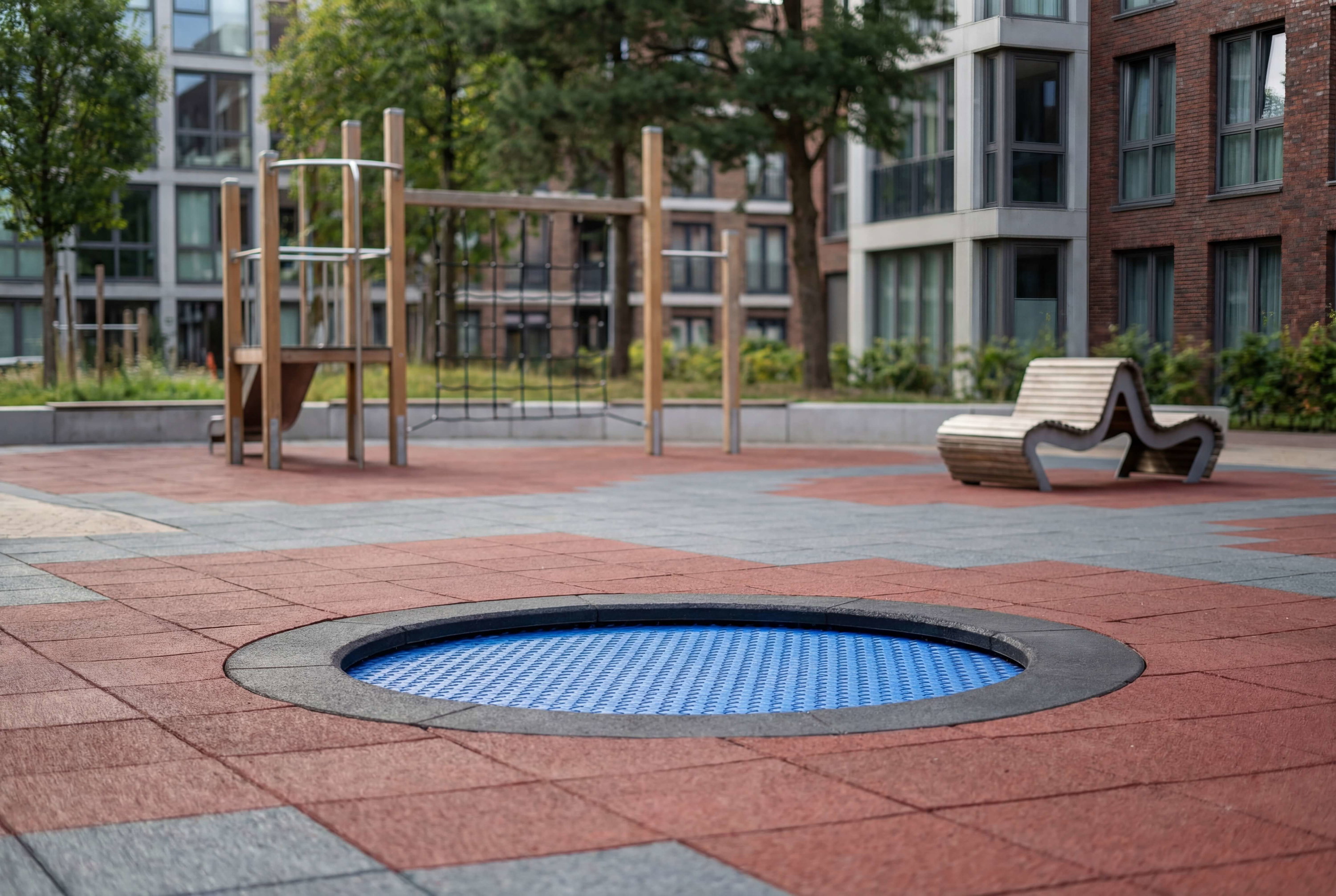 Blauer runder Spielbereich im modernen Wohnhauspark mit Holzspielgeräten und Bänken.