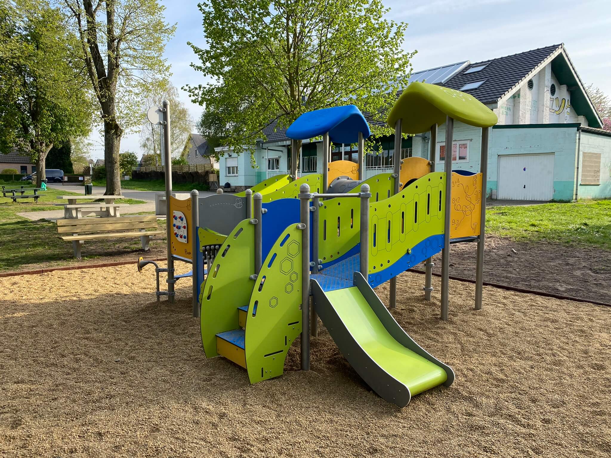 Farbiger Spielplatz mit Rutsche und Klettergerüst auf Sandfläche im Park.