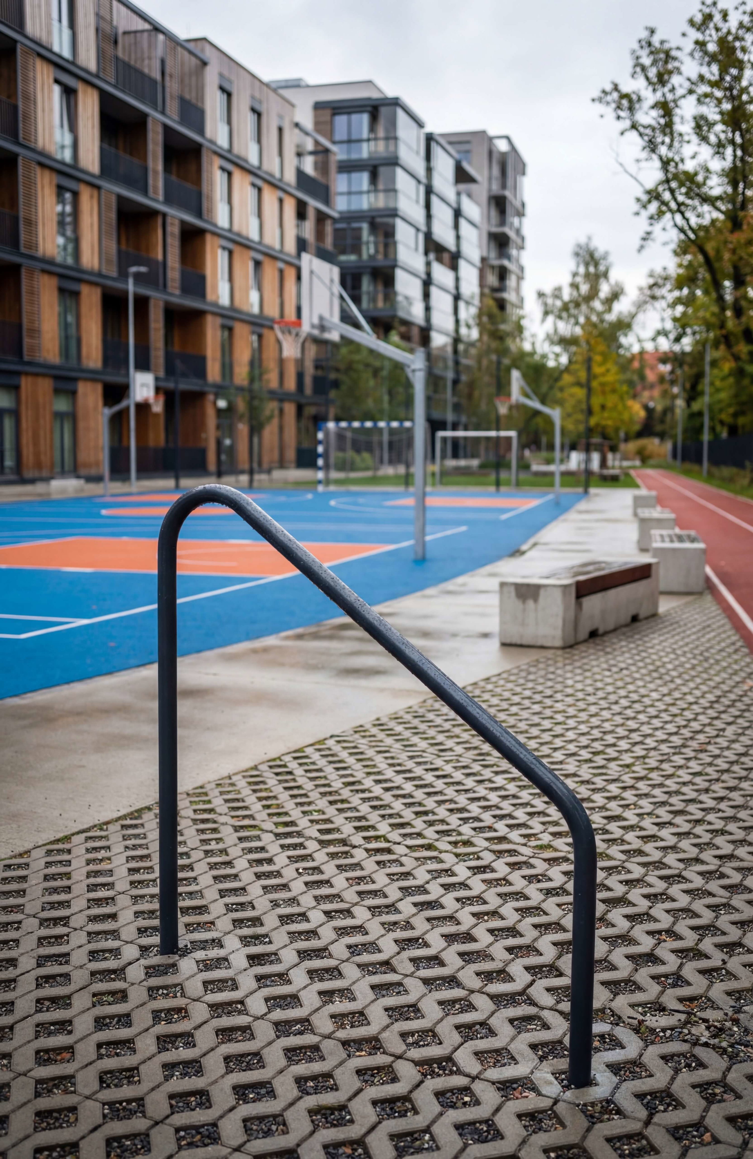 Bleibefläche mit Geländer vor Basketballplatz und modernen Wohnhäusern im Stadtteil.