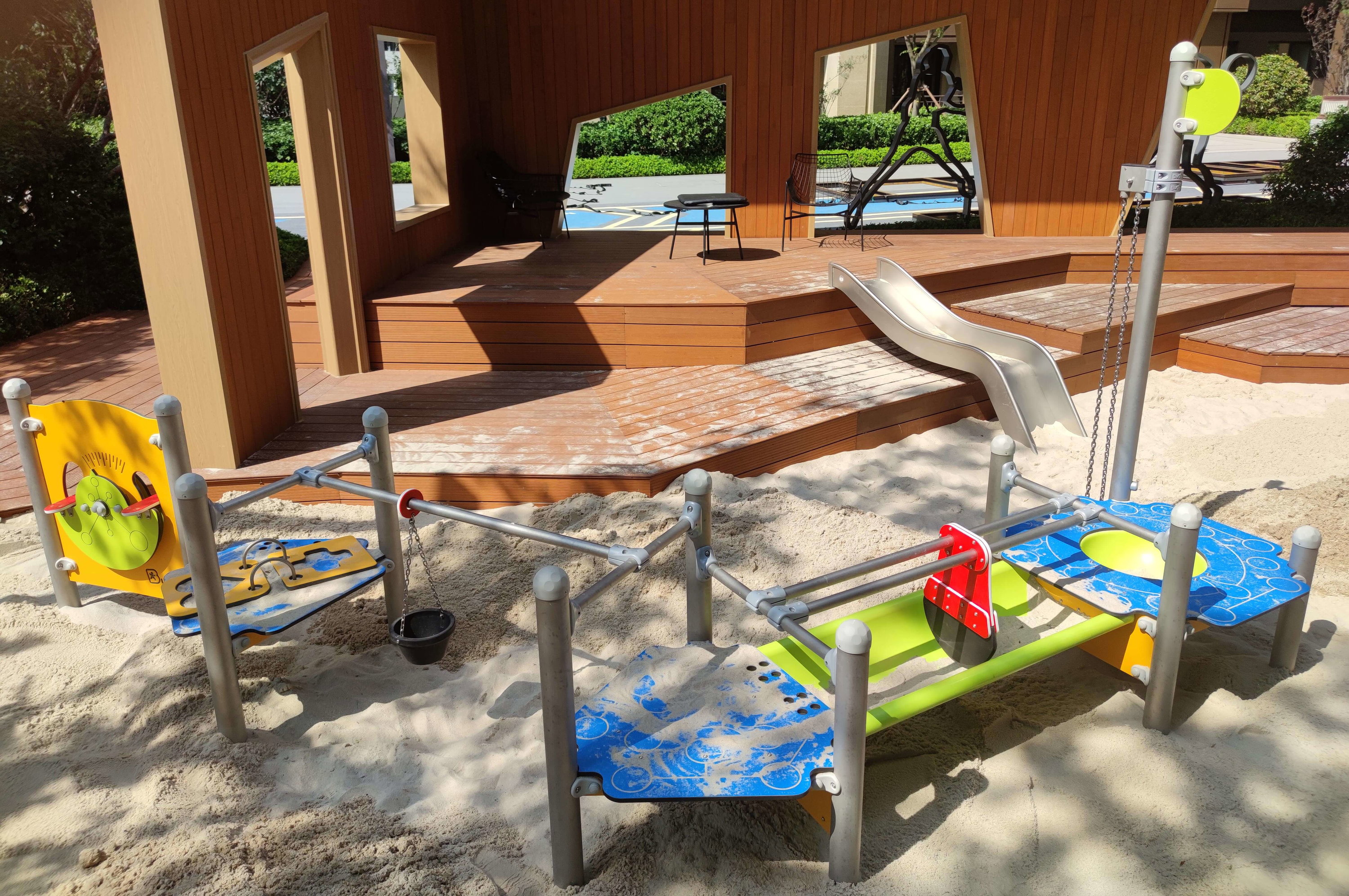 Spielplatz mit Sandkiste und Rutsche vor Holzhaus im Freien.