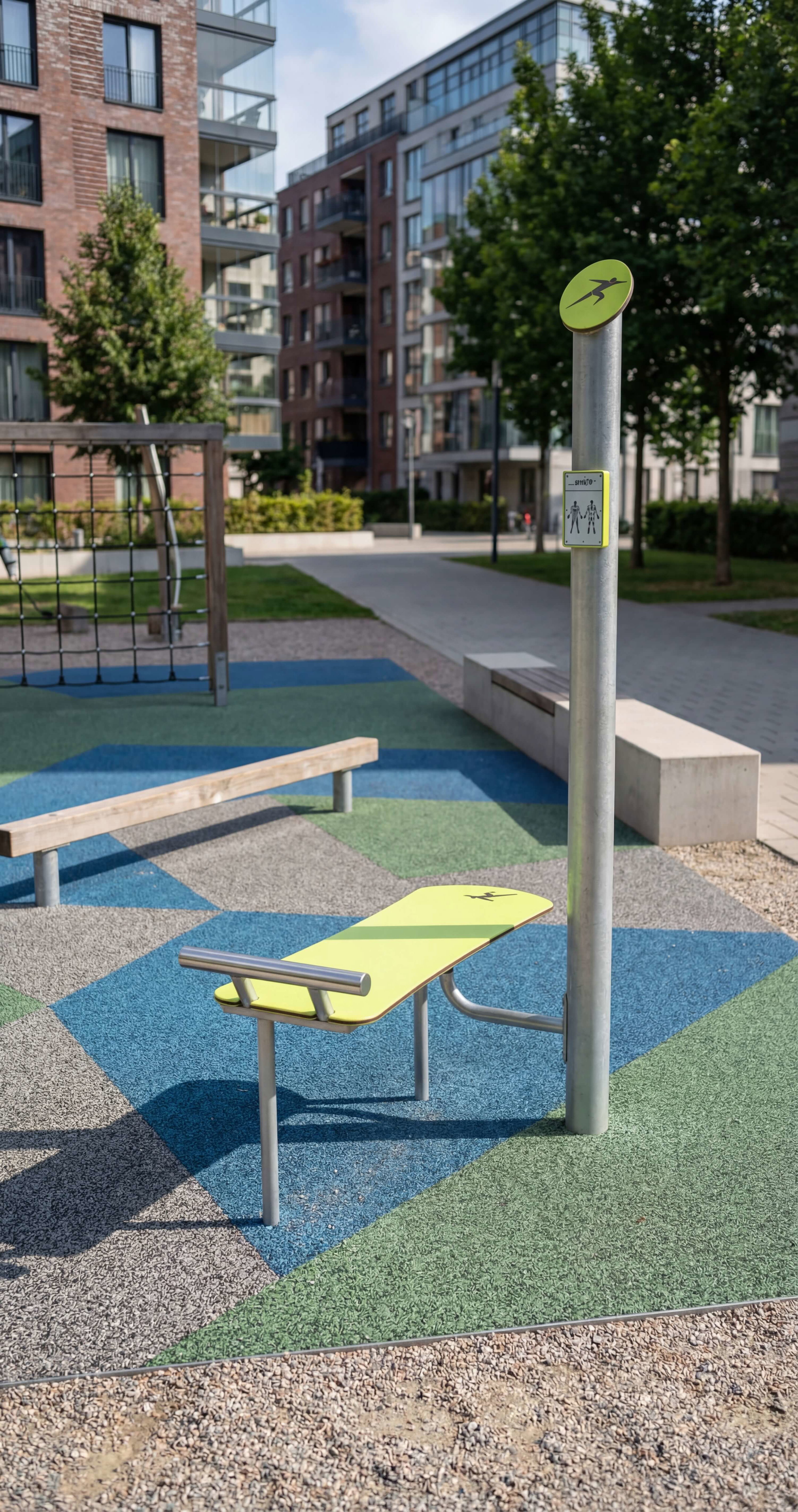Gelber Fitnessbank im städtischen Park mit buntem Boden und Wohnhäusern im Hintergrund.