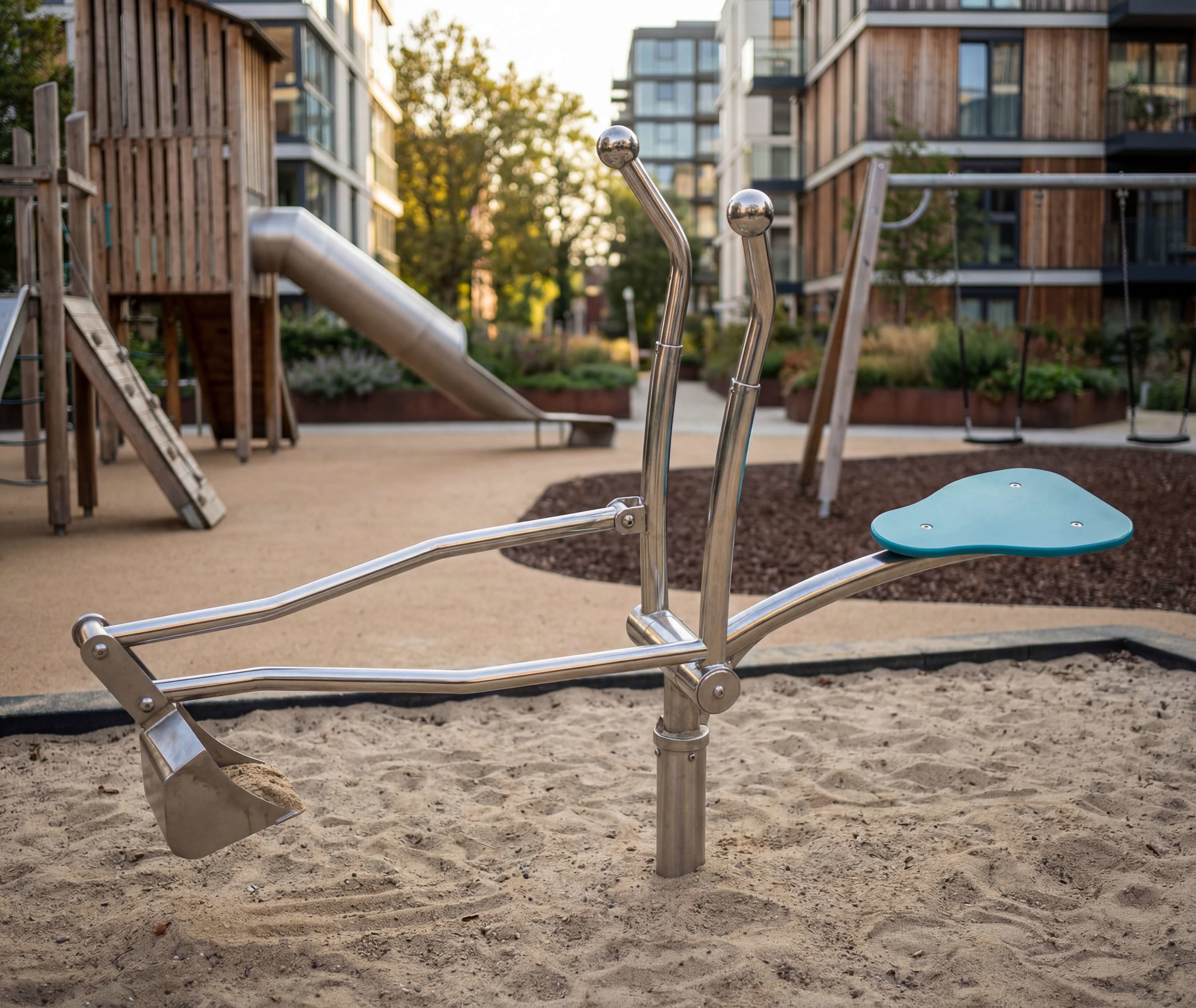 Metallenes Spielgerät im Sandkasten eines modern gestalteten Kinderspielfeldes vor Wohnhäusern.