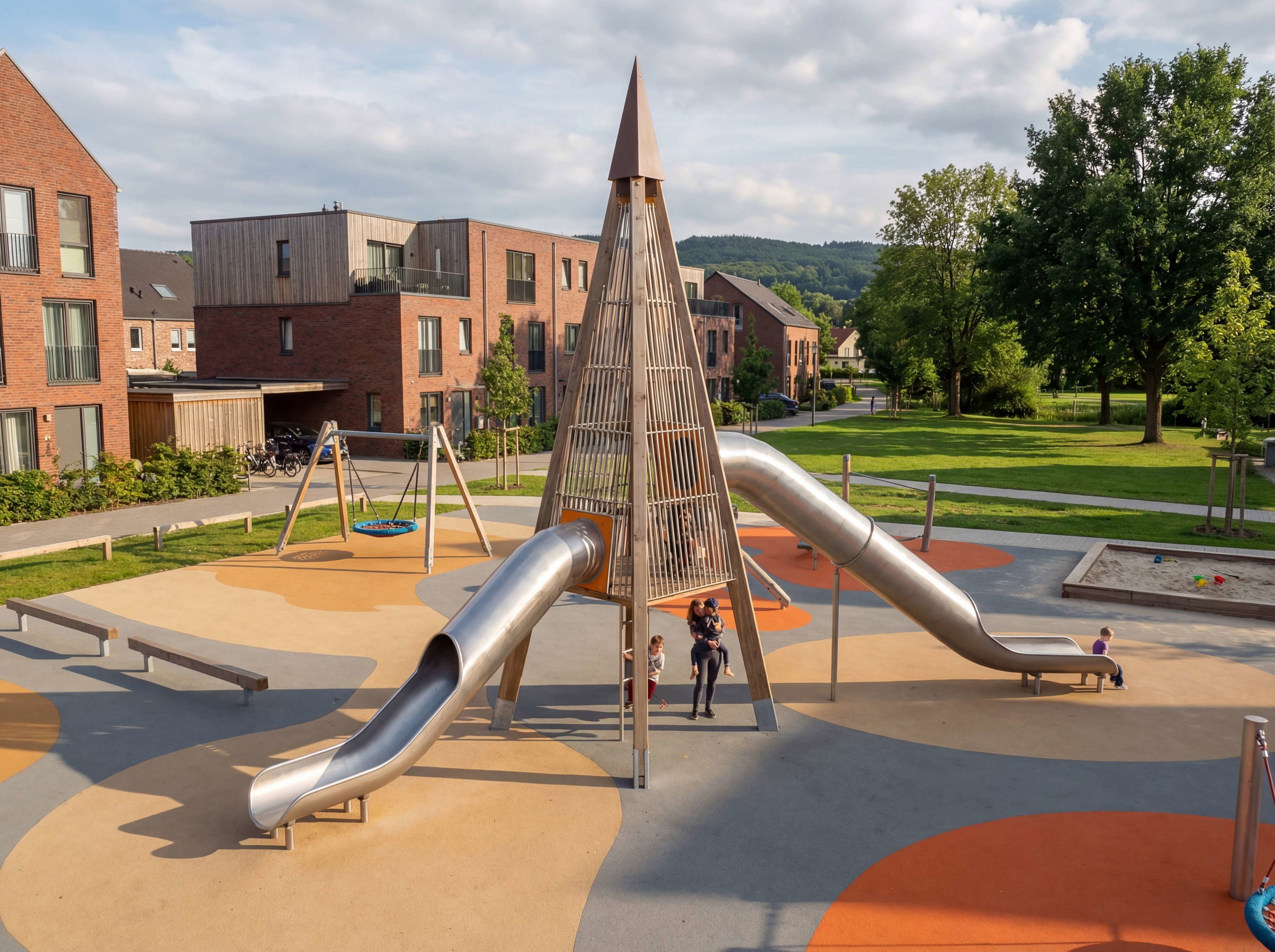 Modern Spielplatz mit Metallschlitten und Kindern vor Wohnhäusern im Grünen.