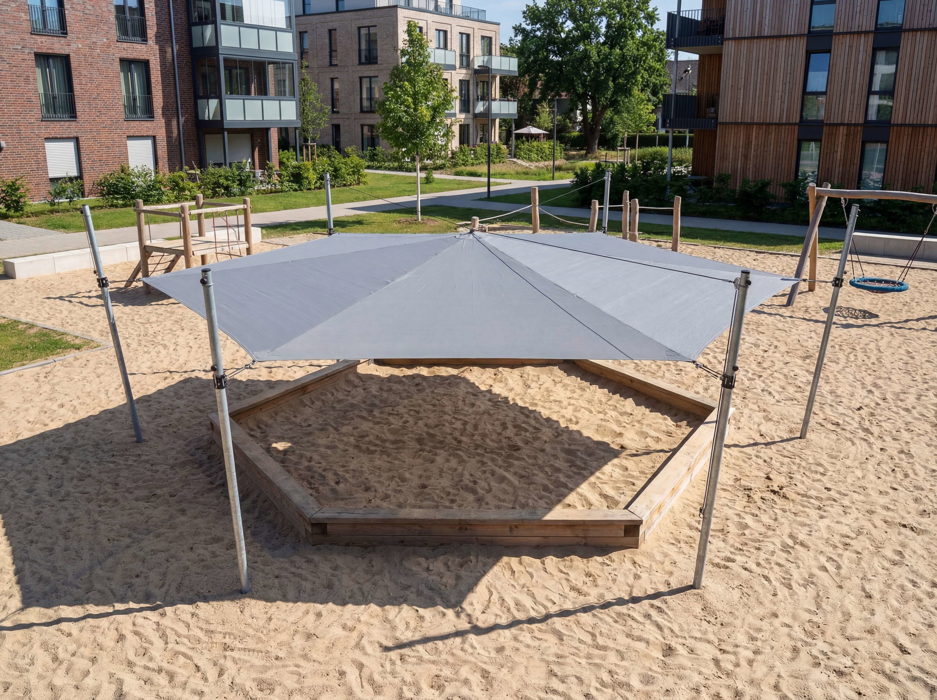 Spielplatz mit Sandkasten und Schutzdach vor modernen Wohnhäusern im Grünen.