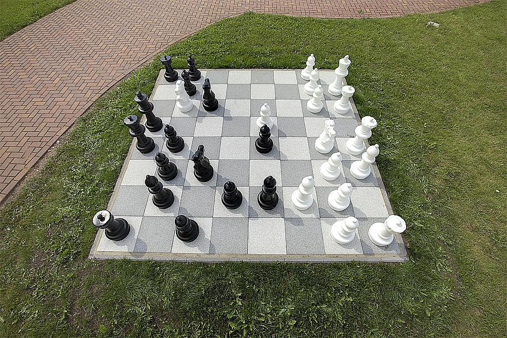 Großes Schachspiel im Garten auf Rasen und Pflastersteinen – Spielsteine stehen bereit für einen Wettkampf.