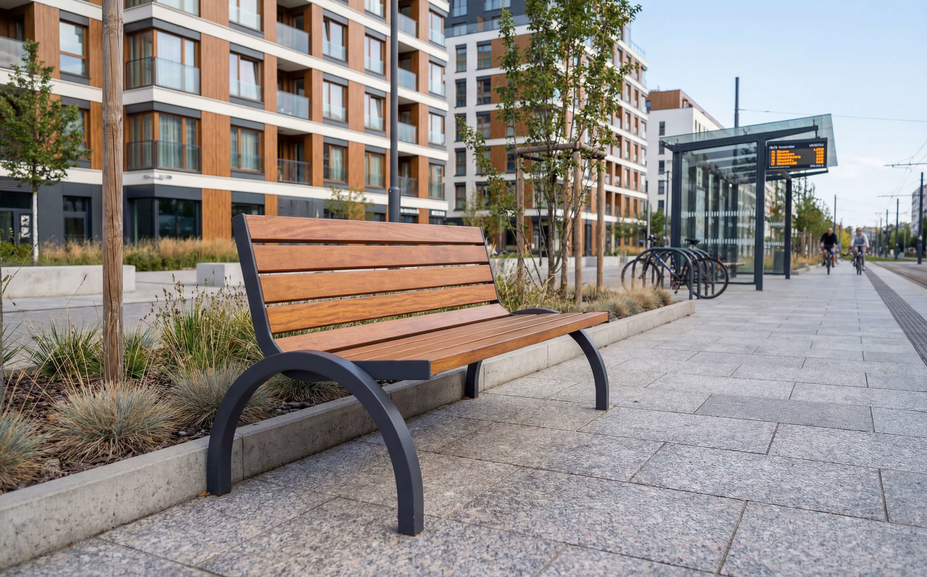 Holzbank am modernen Bahnhof mit Wohnhäusern und Fahrradständer im Hintergrund.