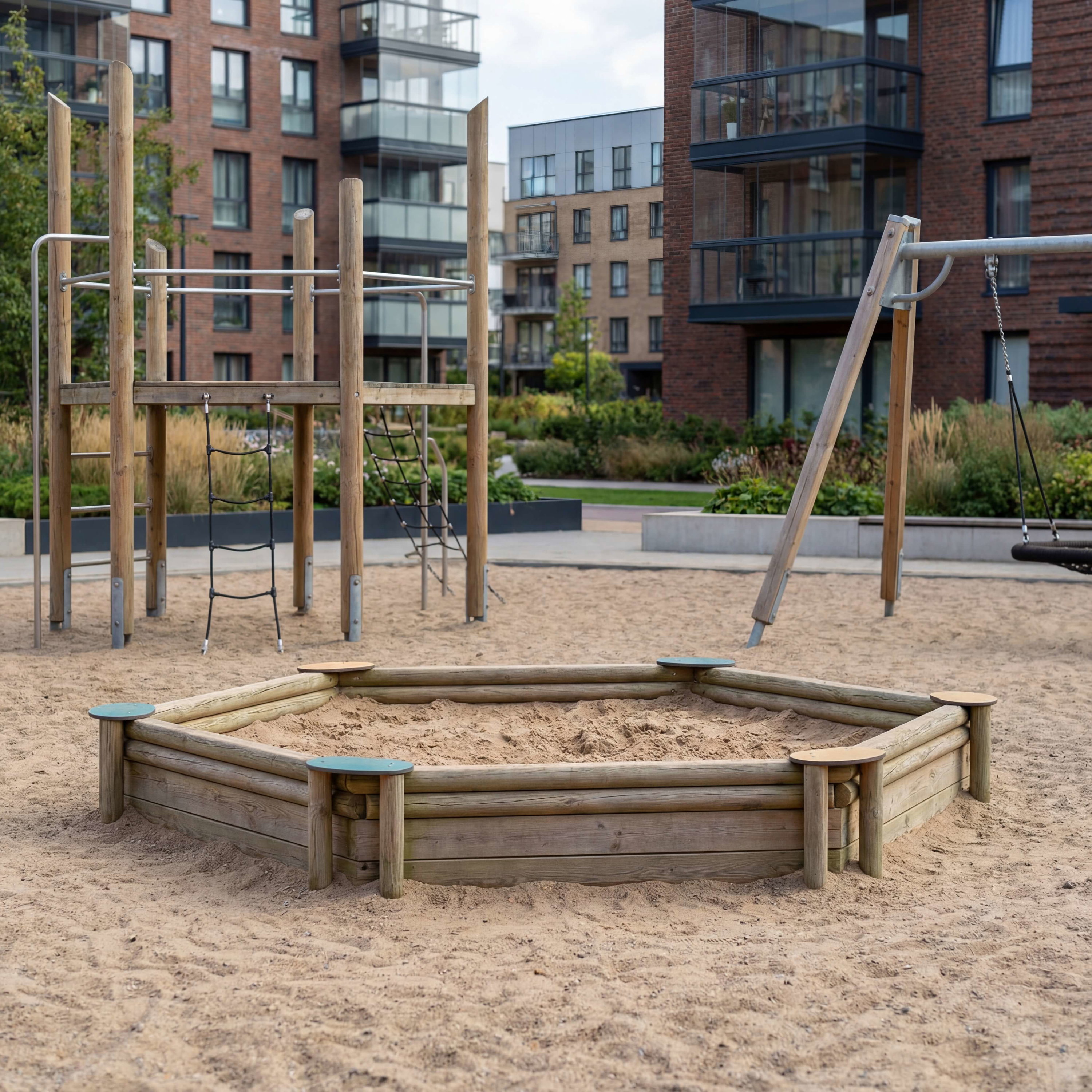 Holzspielplatz mit Sandkasten und Klettergerüst vor modernen Wohnhäusern im Stadtpark.