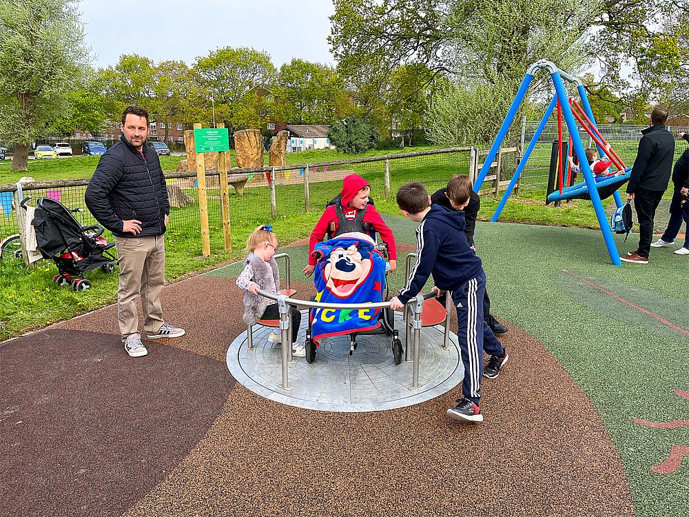 Kinder und Eltern spielen auf einem inklusiven Spielplatz mit Drehplattform und Schaukel.

Inklusions-Spielplatz: Kinder drehen sich gemeinsam – ein Kind im Rollstuhl spielt mit Freude dabei.