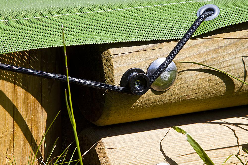 Schwarze Seilbänder mit Metallösen sichern grünes Netz an Holzpfosten im Garten.