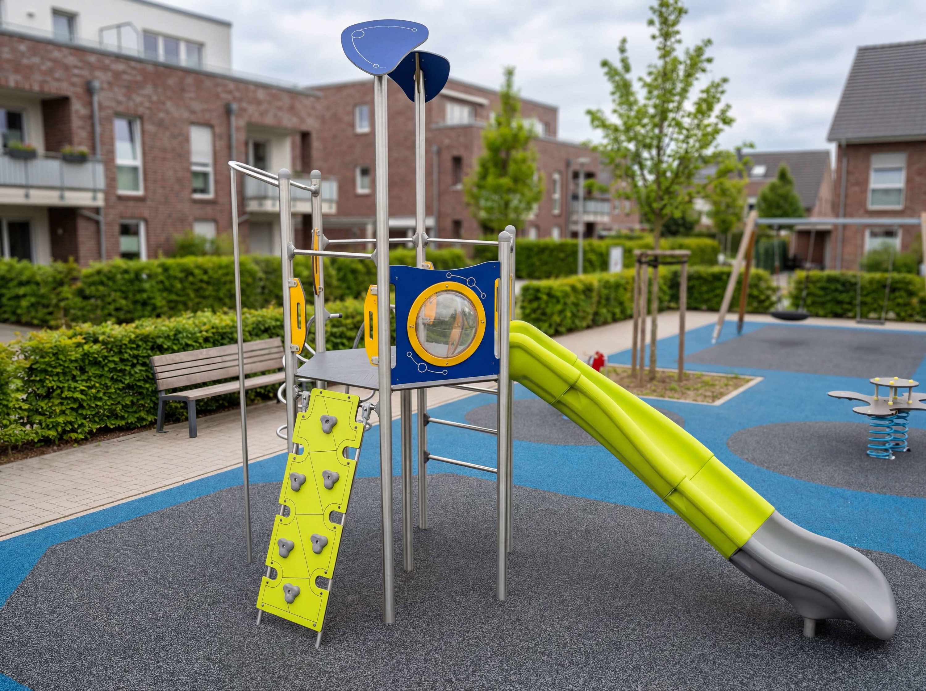 Farbiger Spielplatz mit Rutsche und Kletterwand vor Wohnhäusern im Stadtteil.