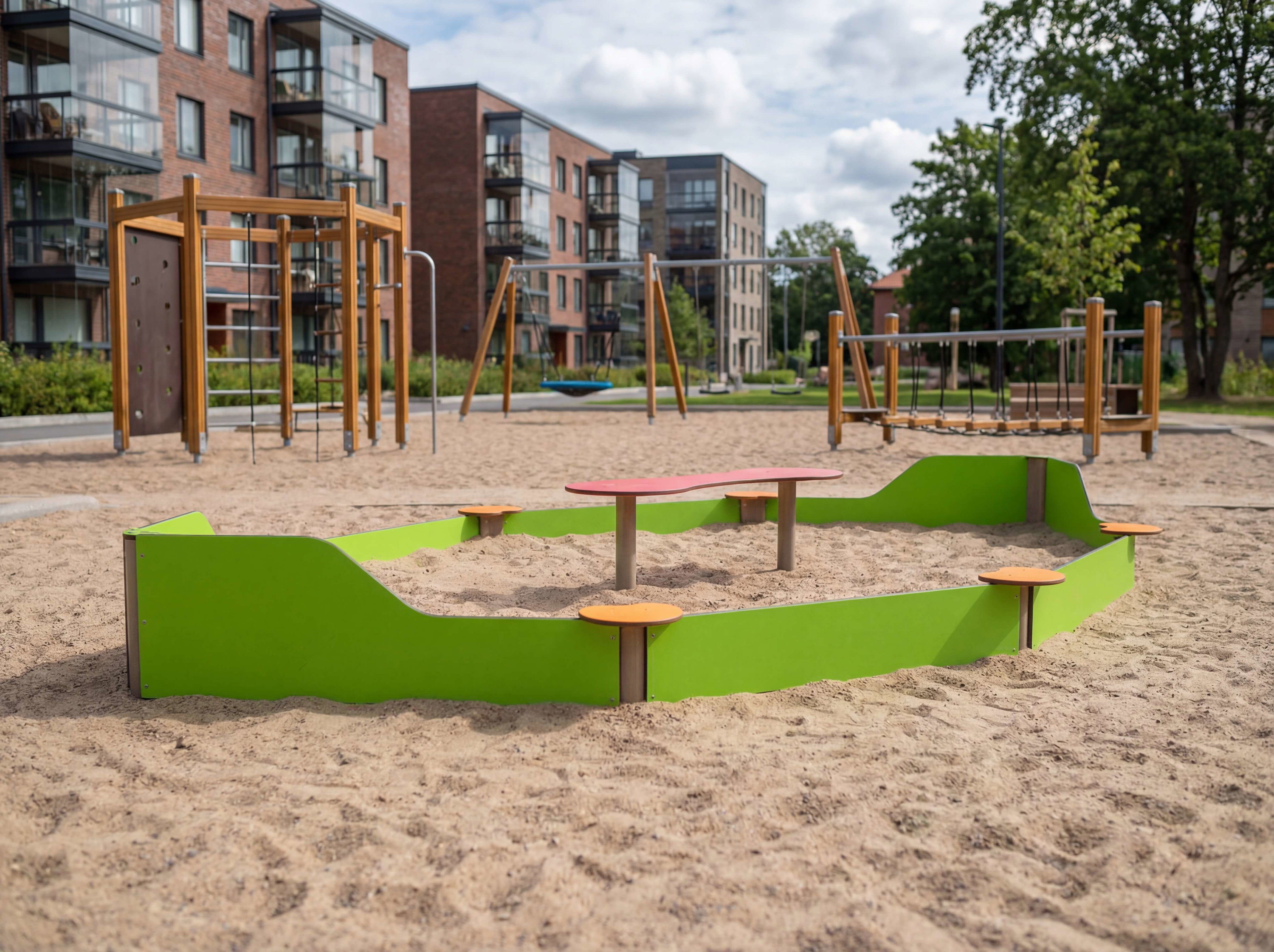Spielplatz mit Sandkasten und Klettergerüst vor modernem Wohnhaus im Grünen.