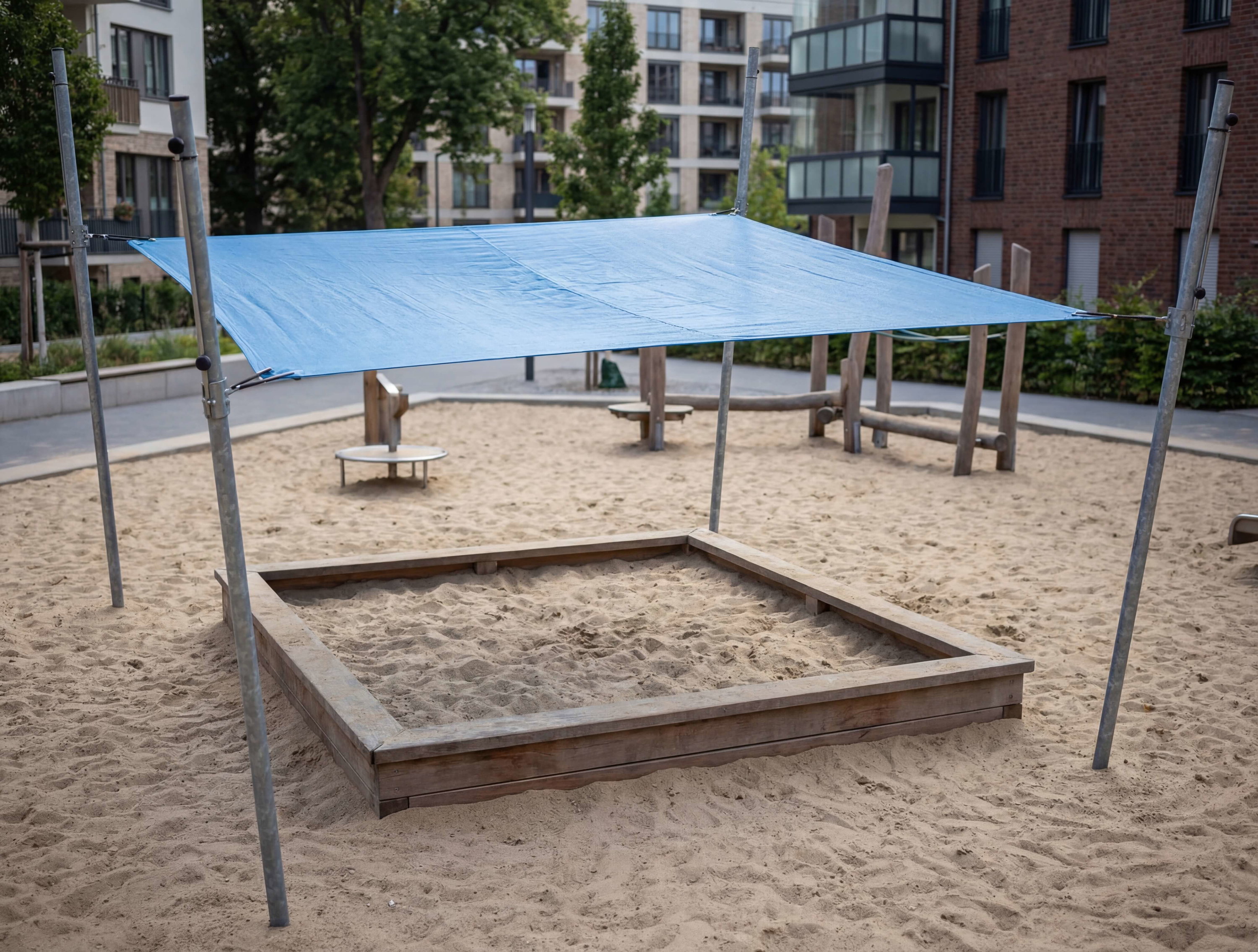 Blauer Schattenspender über Sandkasten im Spielplatz vor Wohnhäusern.