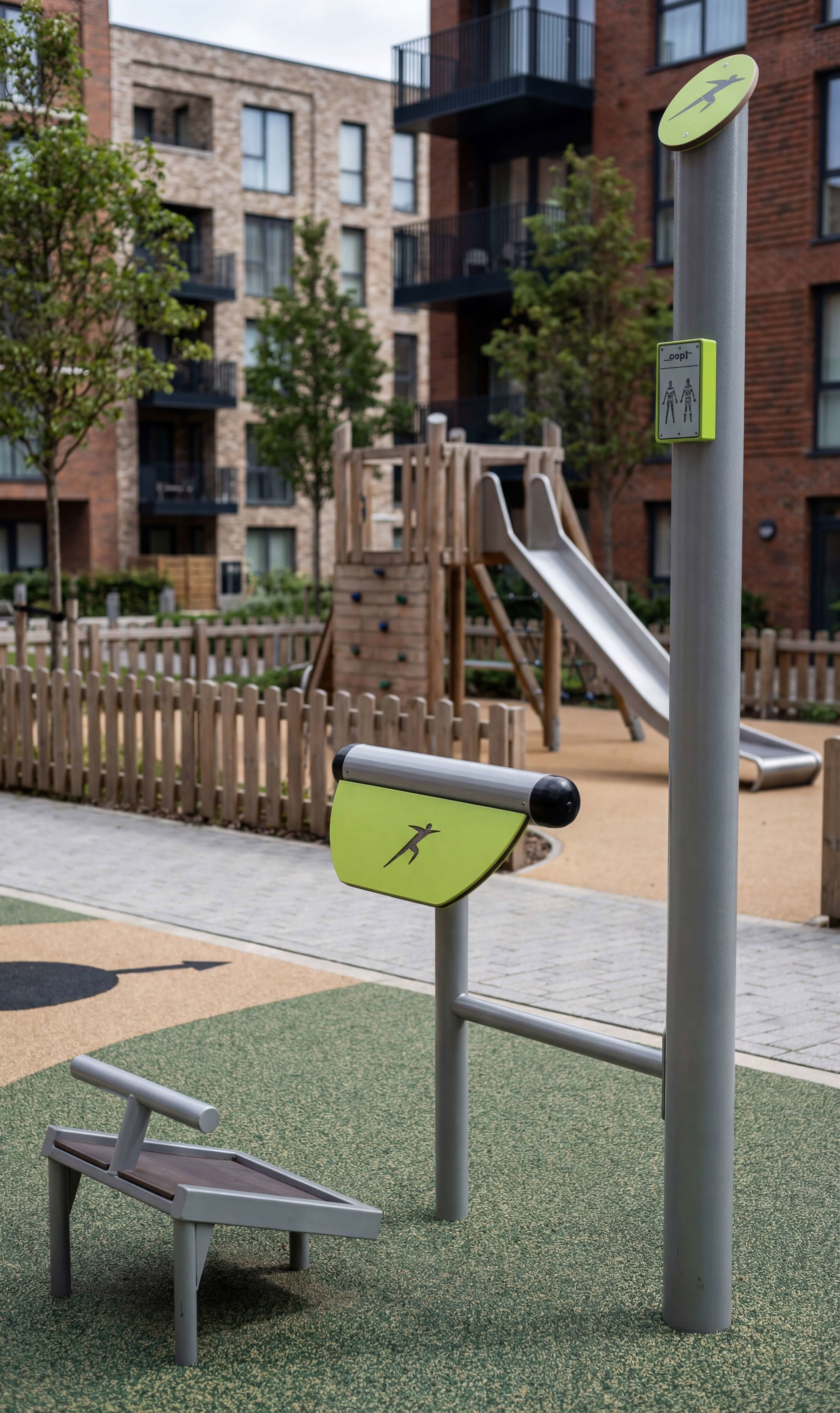 Modern outdoor fitness station with green accents in urban playground area near residential buildings.