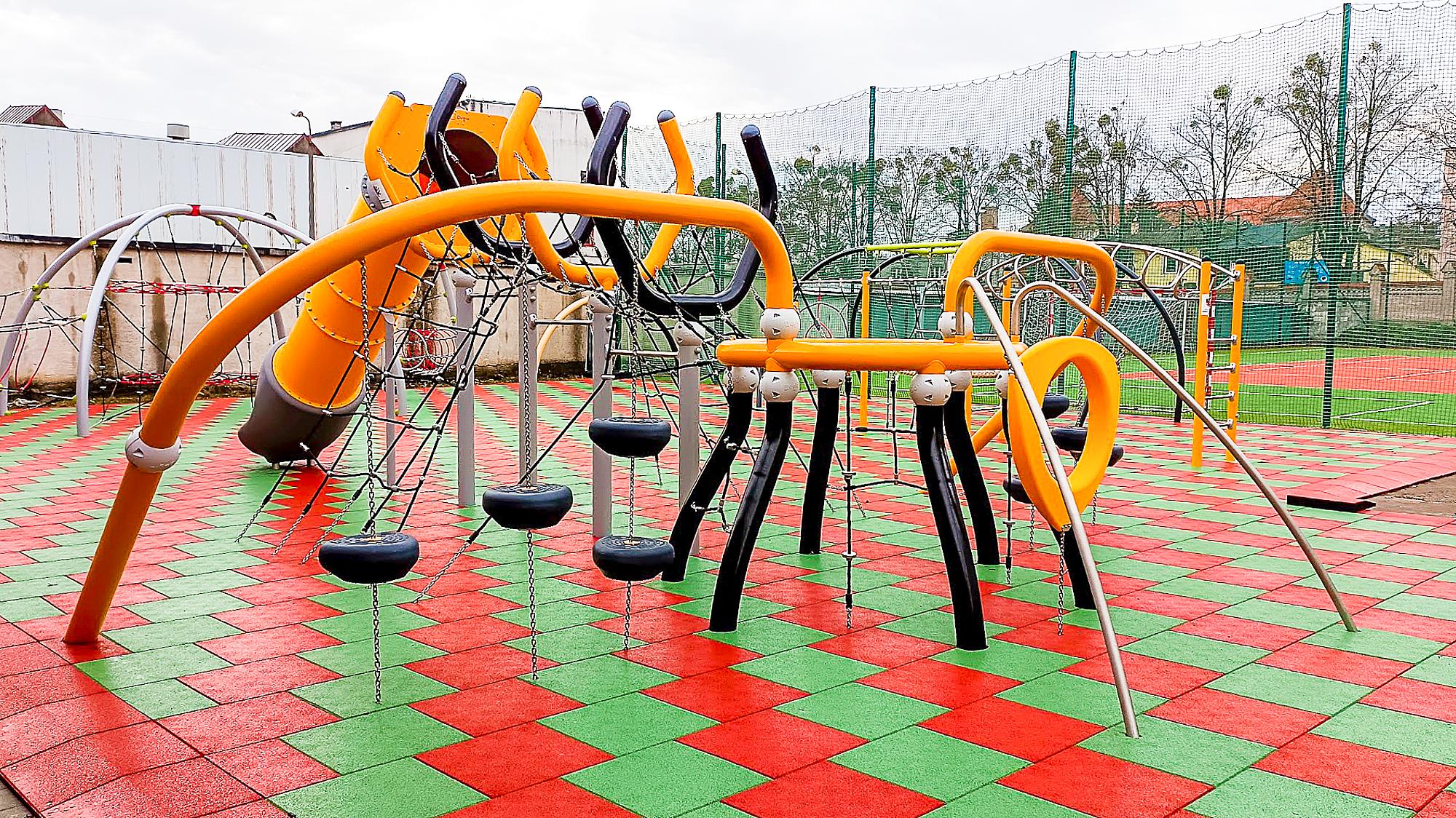 Farbiger Spielplatz mit Rutschen und Klettergerüsten auf rotem-und-grünem Bodenbelag.