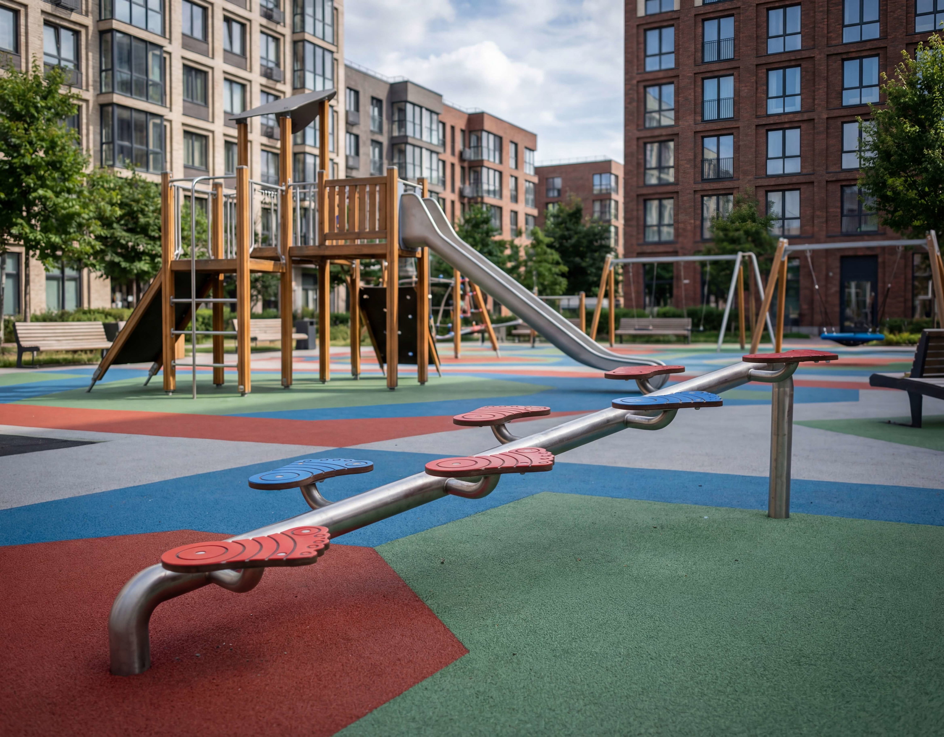 Bunte Spielplatzanlage mit Schaukel und Rutsche vor modernen Wohnhäusern.