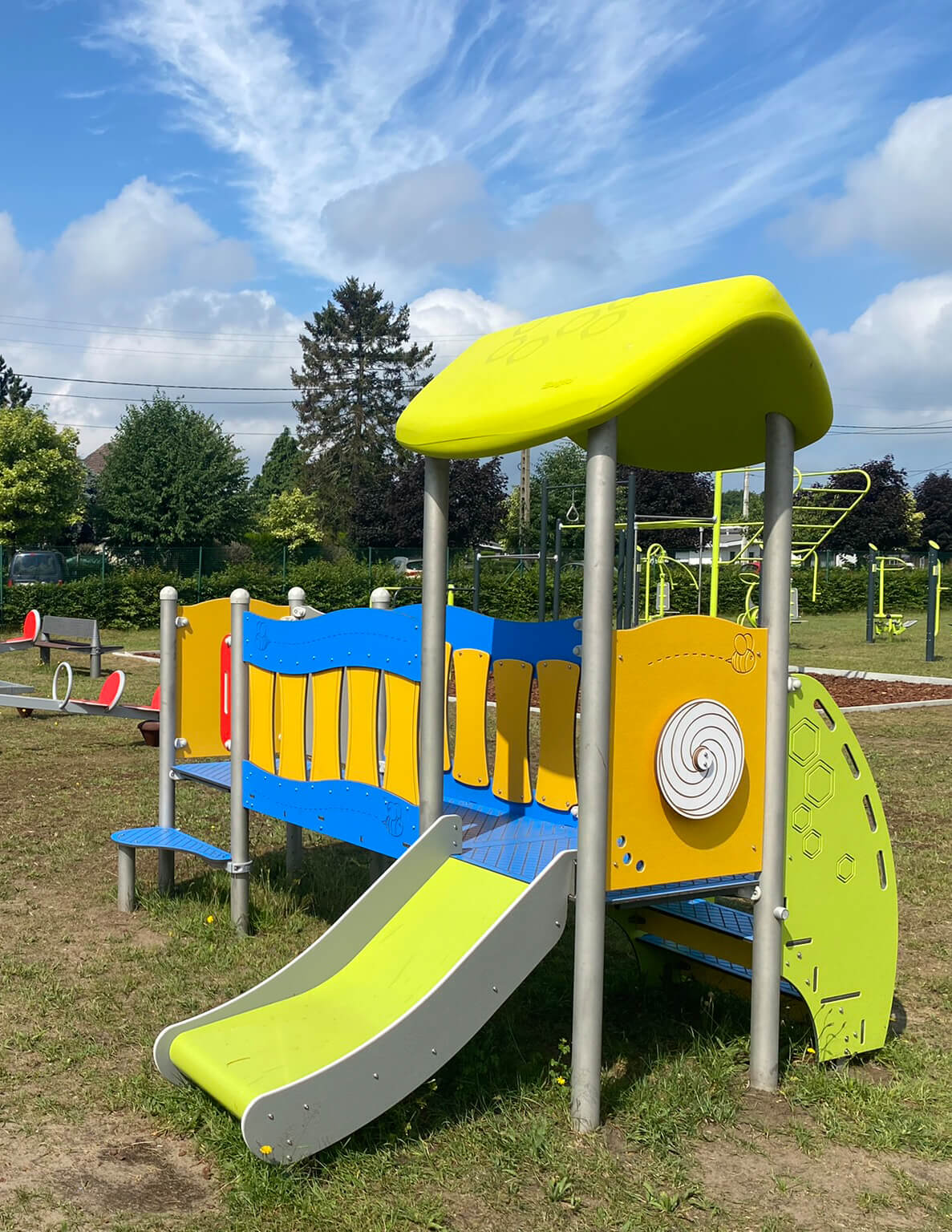 Bunte Spielanlage mit Rutsche und Dach im Park unter blauem Himmel.